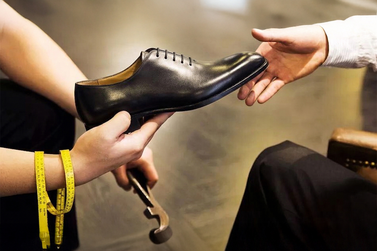製鞋師傅將黑色手工牛津鞋交付給顧客，呈現訂製皮鞋專人服務體驗