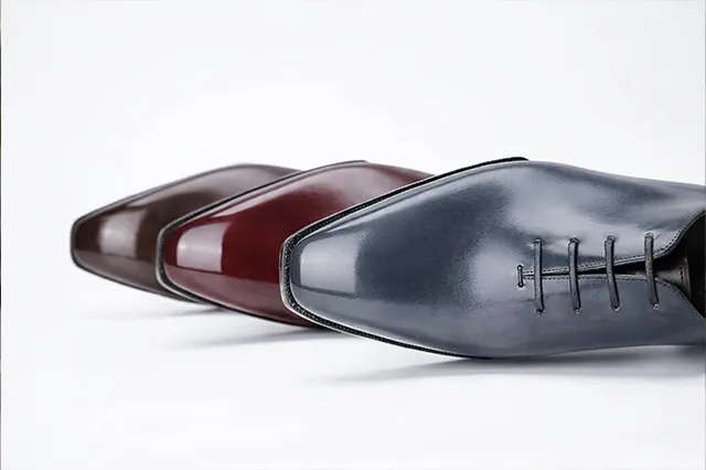 三雙手工皮鞋以橫向排列展示，包含灰藍色、酒紅色與深棕色款式，呈現高級訂製皮鞋的光澤與細膩工藝